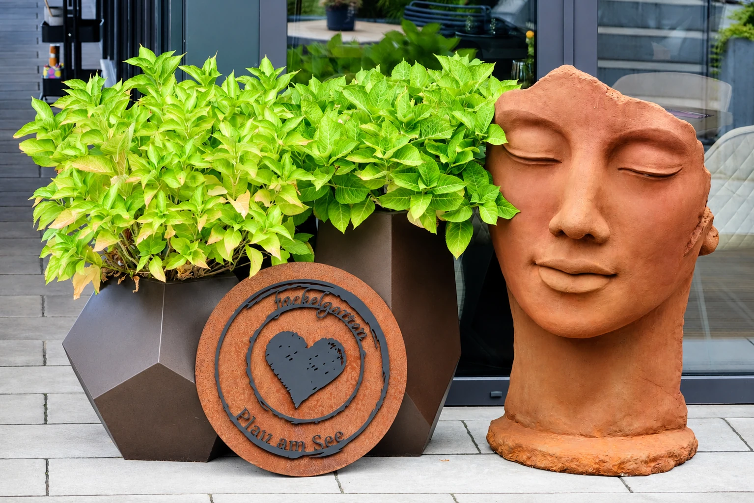 Terrakotta-Kopf-Skulptur und Fackelgarten-Schild mit Herz auf der Terrasse in Plau am See