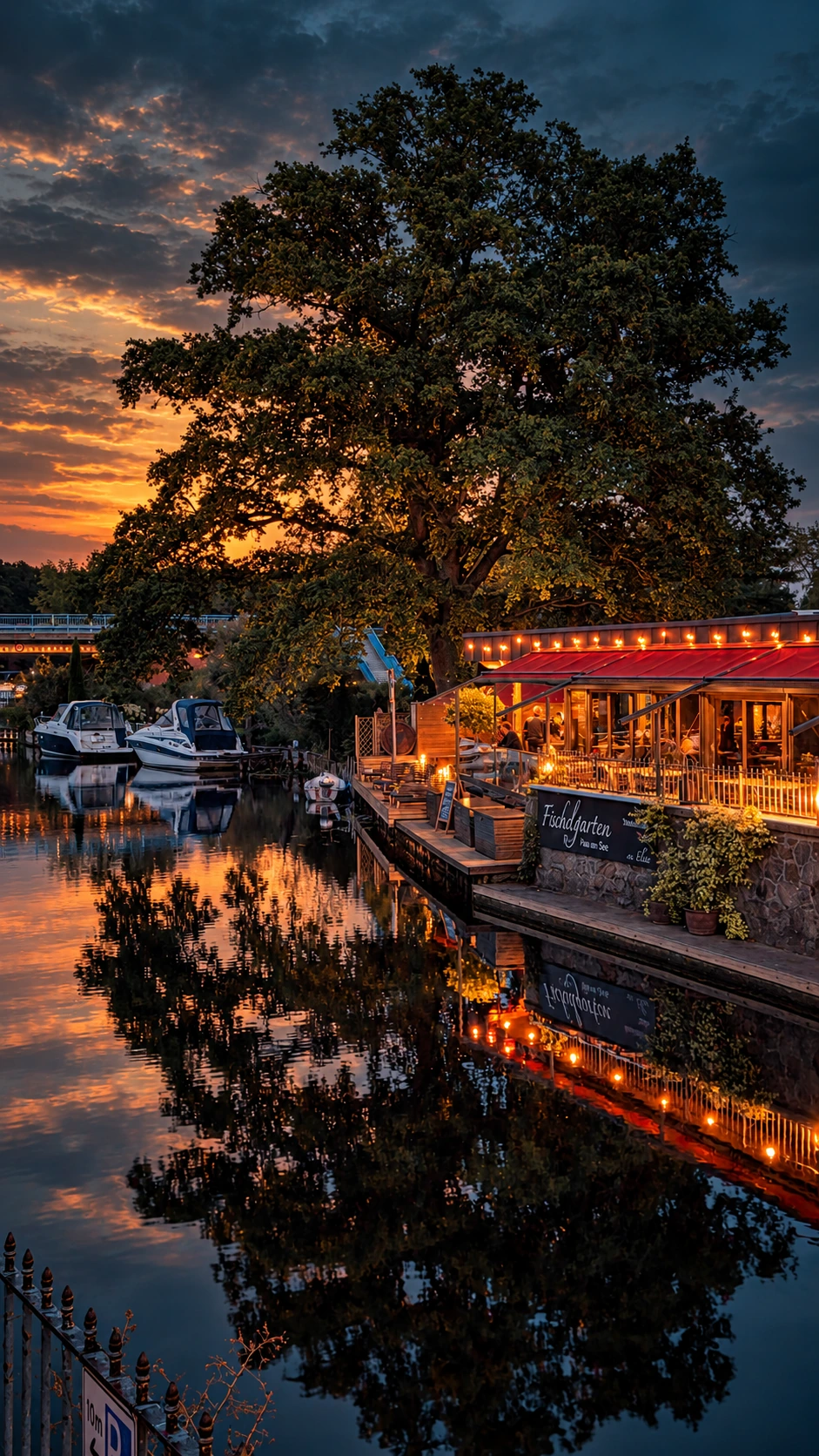 Fackelgarten am Abend: rote Markisen, warmes Licht, Spiegelung im Wasser der Elde, Boote und dramatischer Himmel